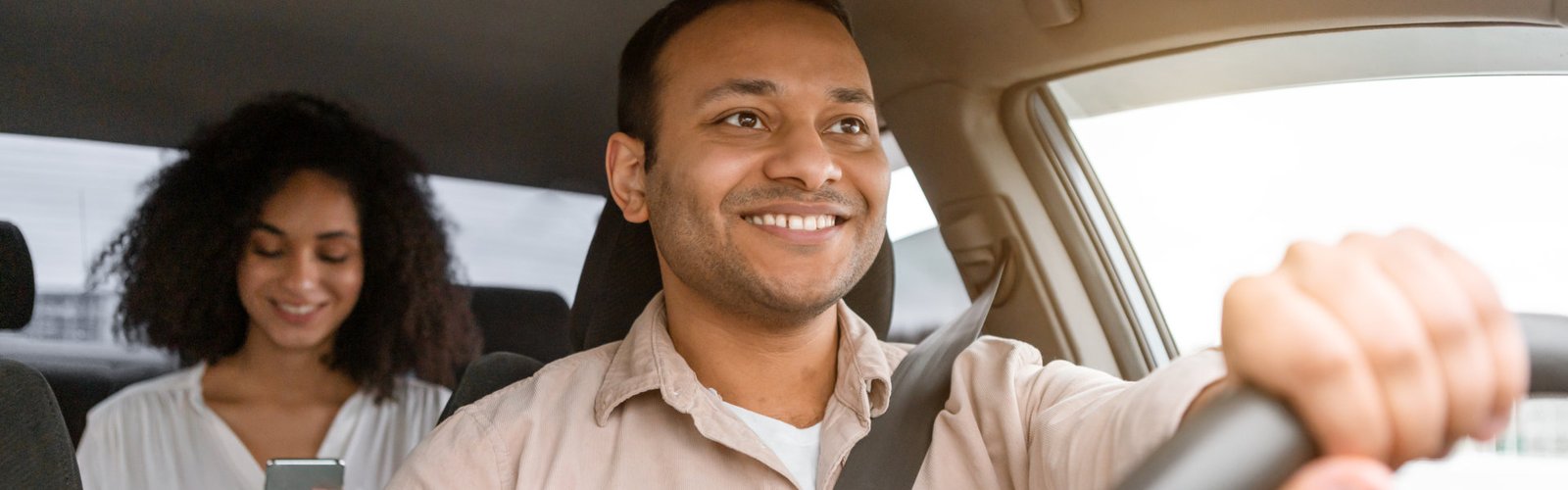 A driver is focused on the road while a passenger in the back seat uses a smartphone